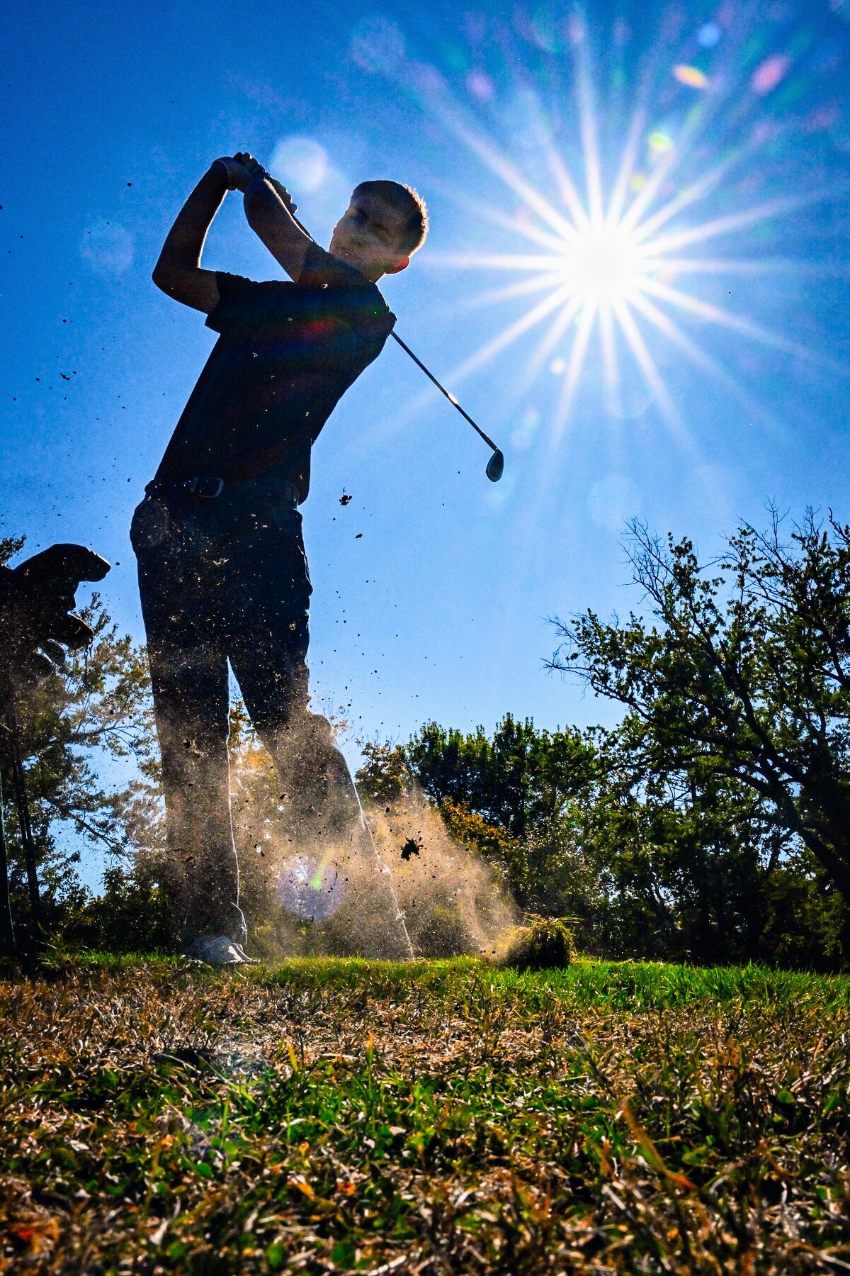 Multiple action shots of a golfer swinging a club against a bright blue sky with dirt and grass flying through the air.