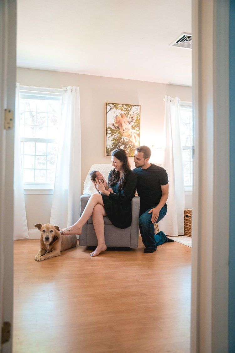 A couple sits on hardwood floor in empty room with dog while viewed through multiple doorway frames.