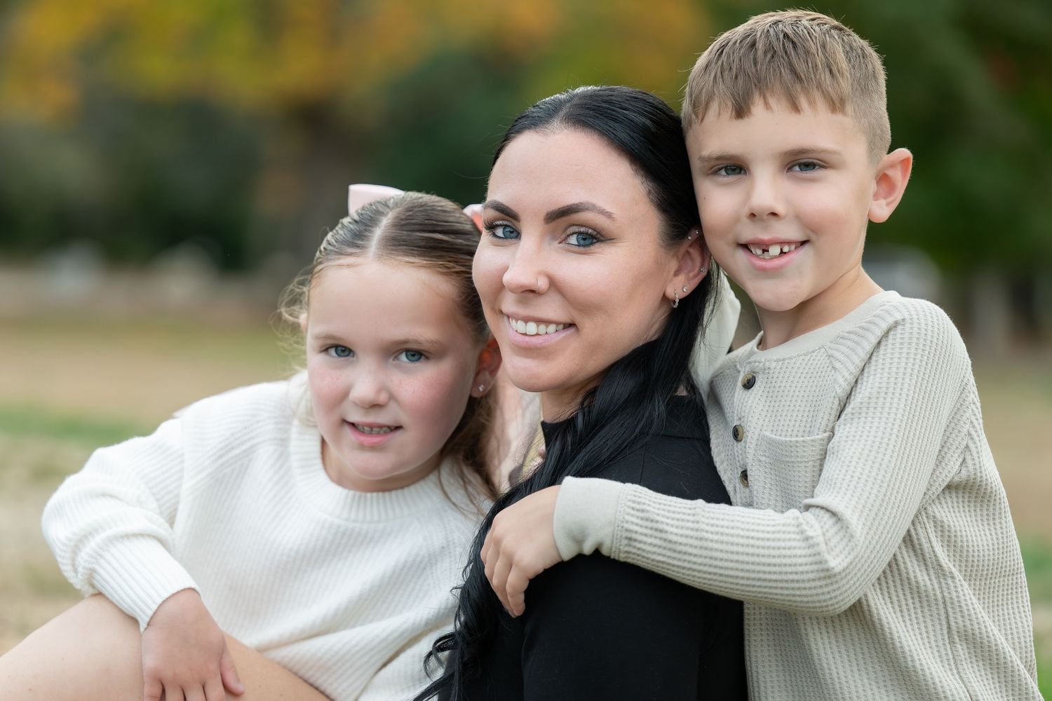 A family of three smiling together outdoors during a casual autumn photo session.