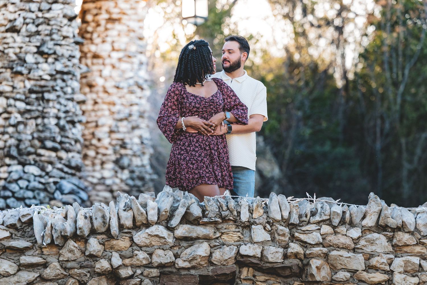 Couple shares romantic moments against rustic stone wall backdrop during outdoor engagement photo session.