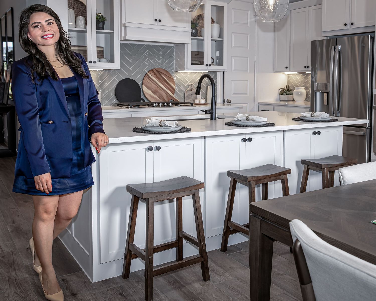 Modern white kitchen features elegant bar stools and pendant lighting along a spacious quartz island counter.