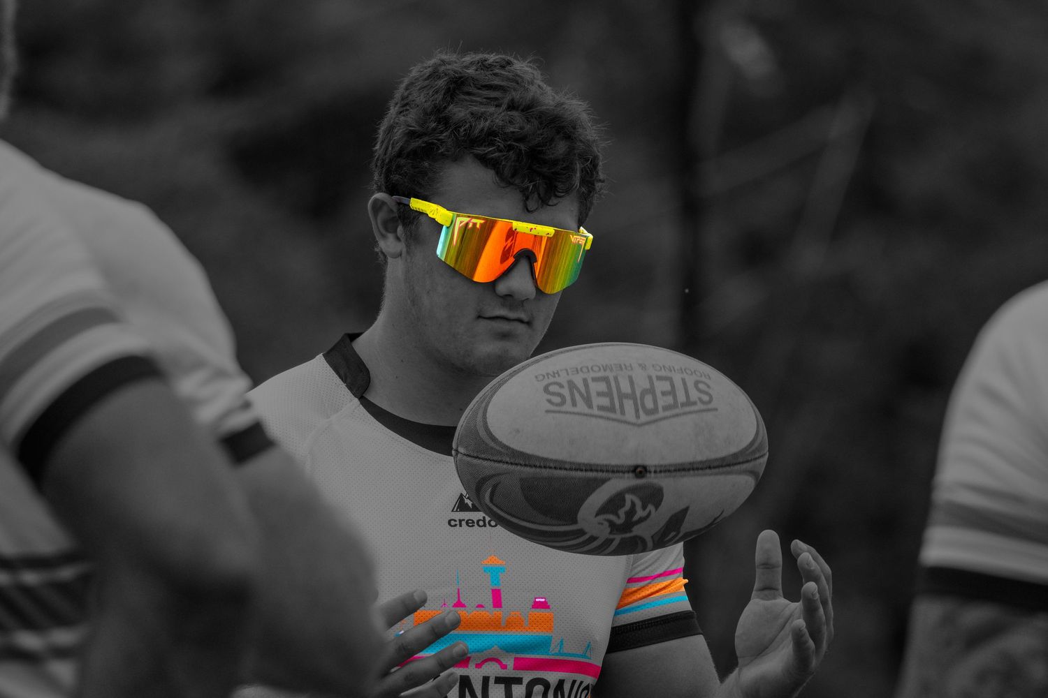 Rugby player in black and white photo wearing colorful sunglasses holding a Stephens rugby ball.