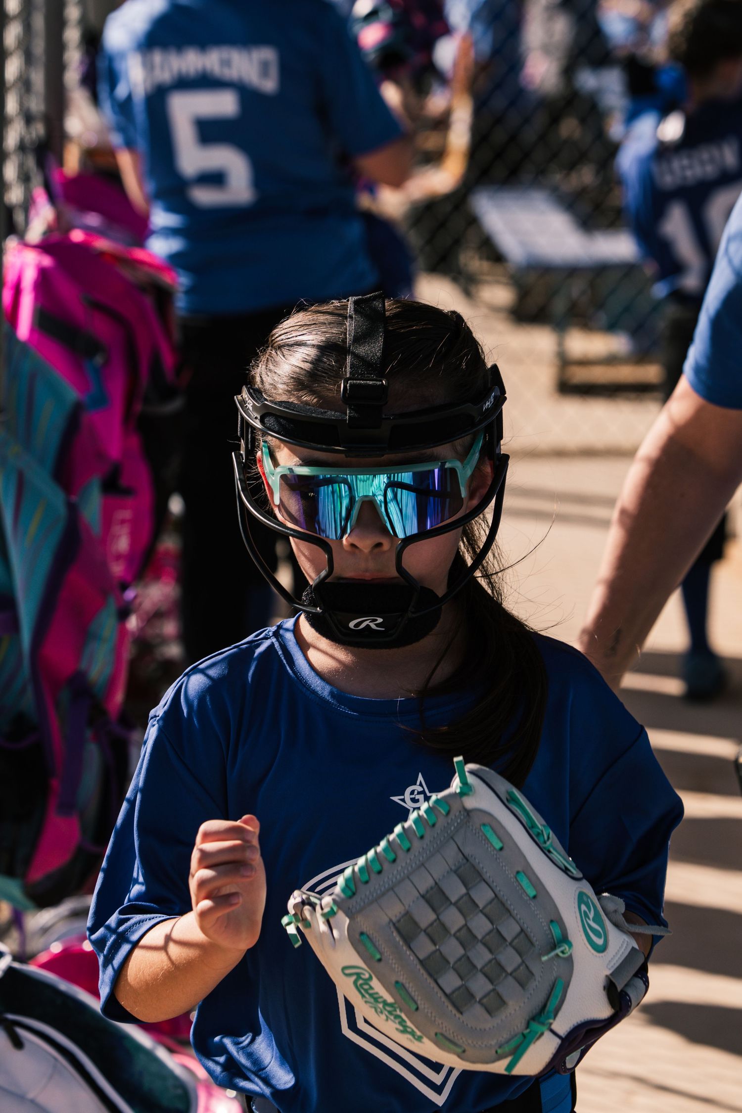 Young girl in blue softball uniform, Rawlings batting helmet, and glove ready to play at a youth softball game.