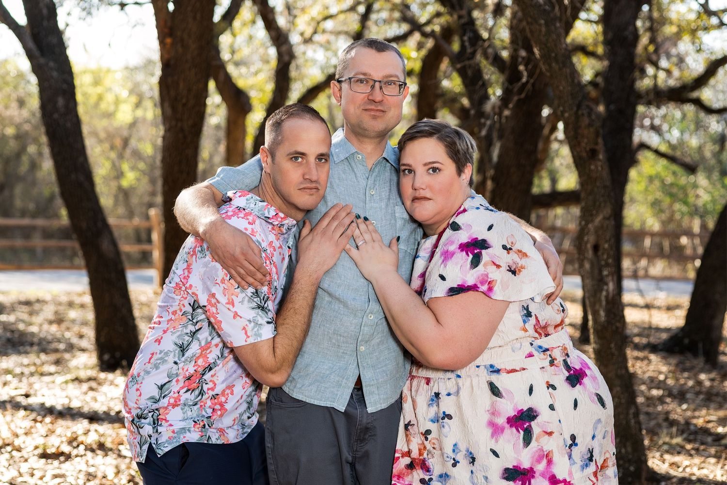 A family portrait of three people standing together in a natural outdoor setting.