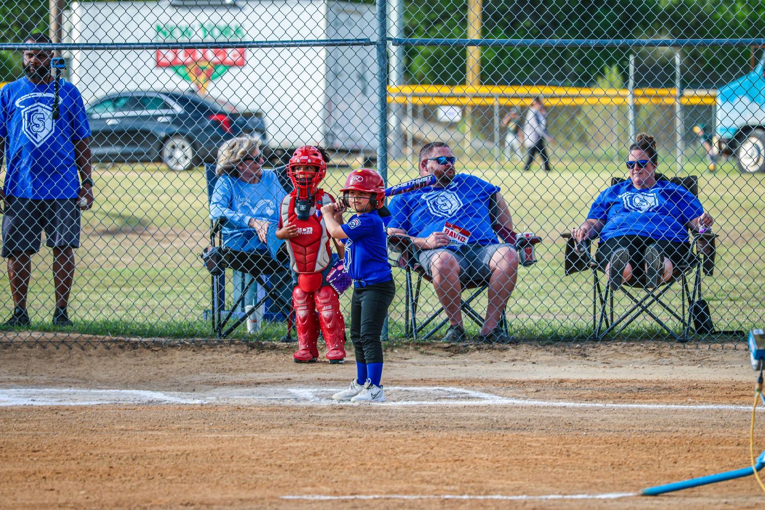 Young softball batter at home plate with catcher and umpire during a youth league game on a green field.