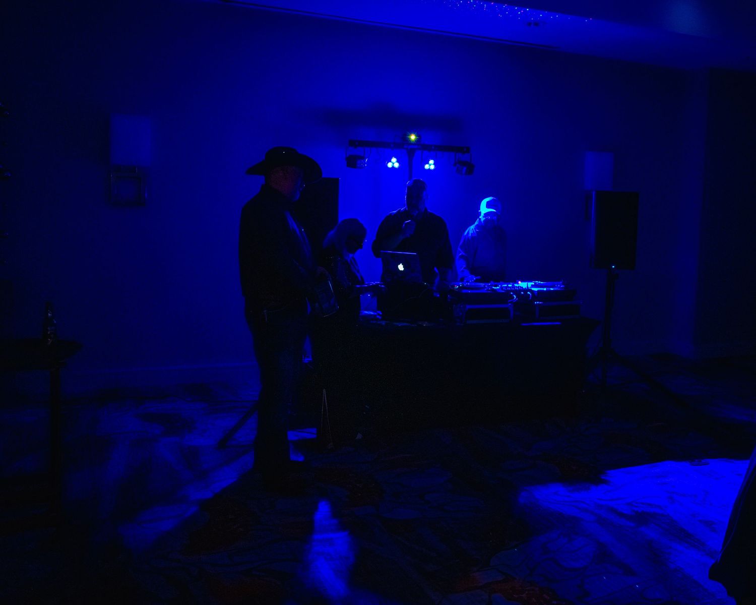 DJ performing at a dark blue-lit nightclub event with atmospheric lighting and music equipment on stage.