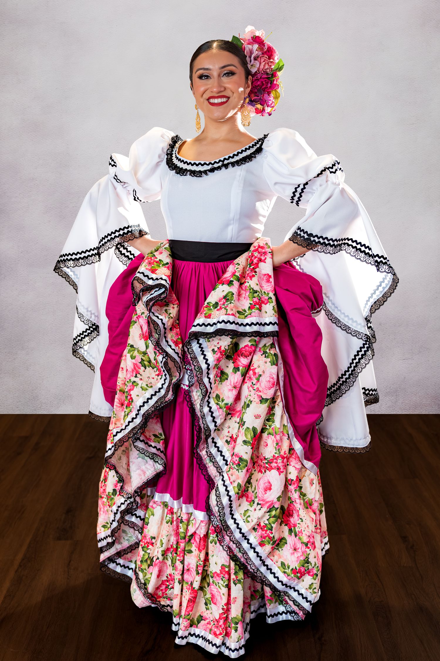Traditional Mexican folk dancer wearing a vibrant pink and floral dress with white ruffled sleeves performs a twirling motion.