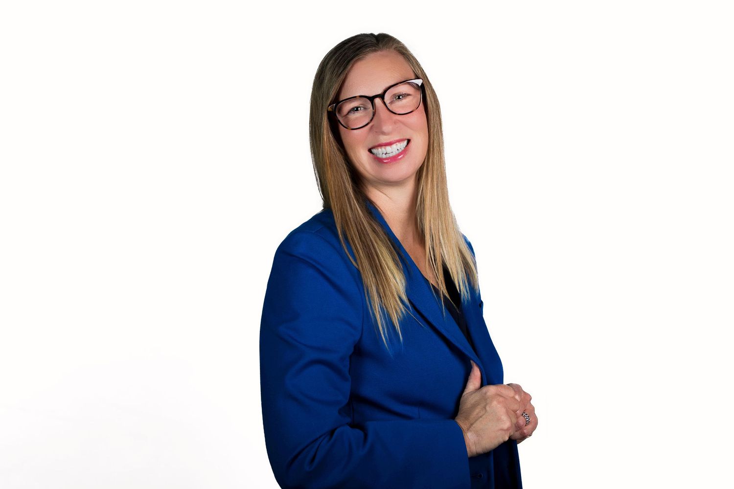 Professional headshot of someone in a royal blue blazer and glasses smiling warmly against a white background.