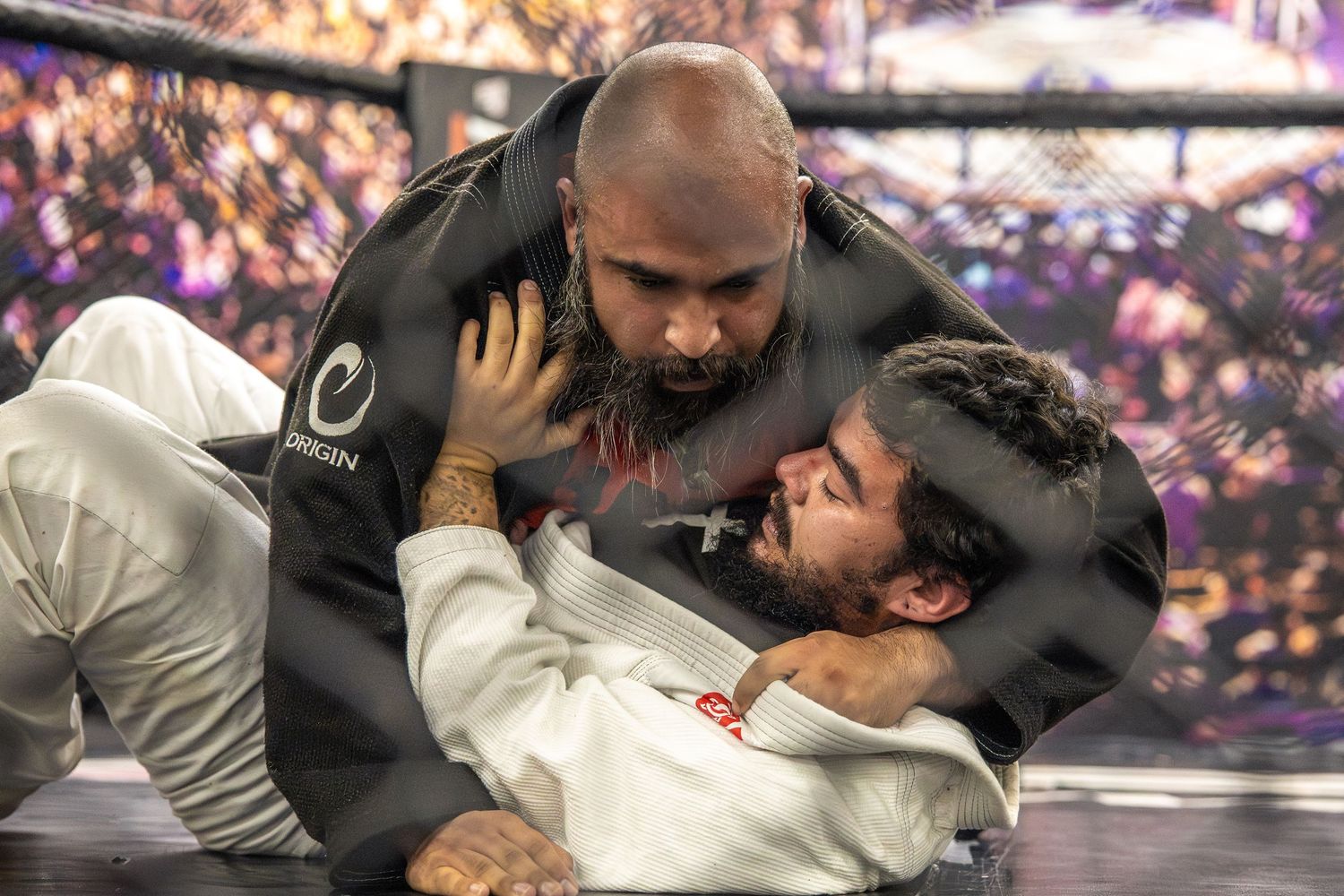 Two MMA fighters in close ground combat, one athlete in a black gi applying pressure in a UFC Gym match.