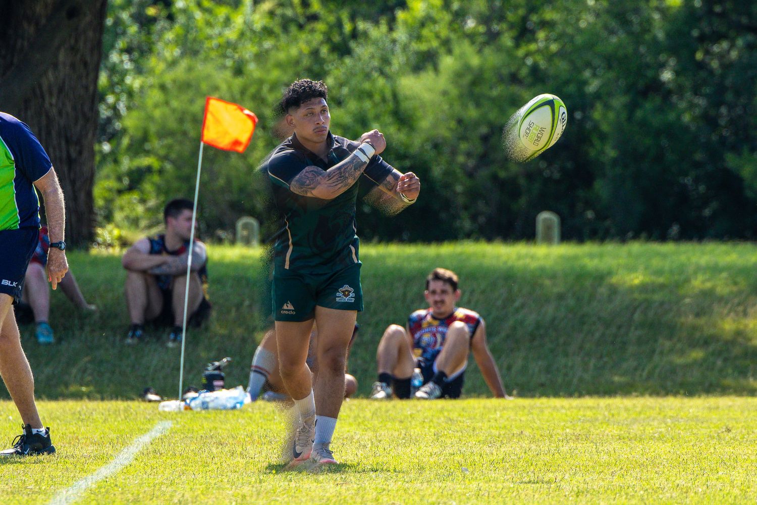Rugby player passing ball during outdoor training session on green field with teammates watching.