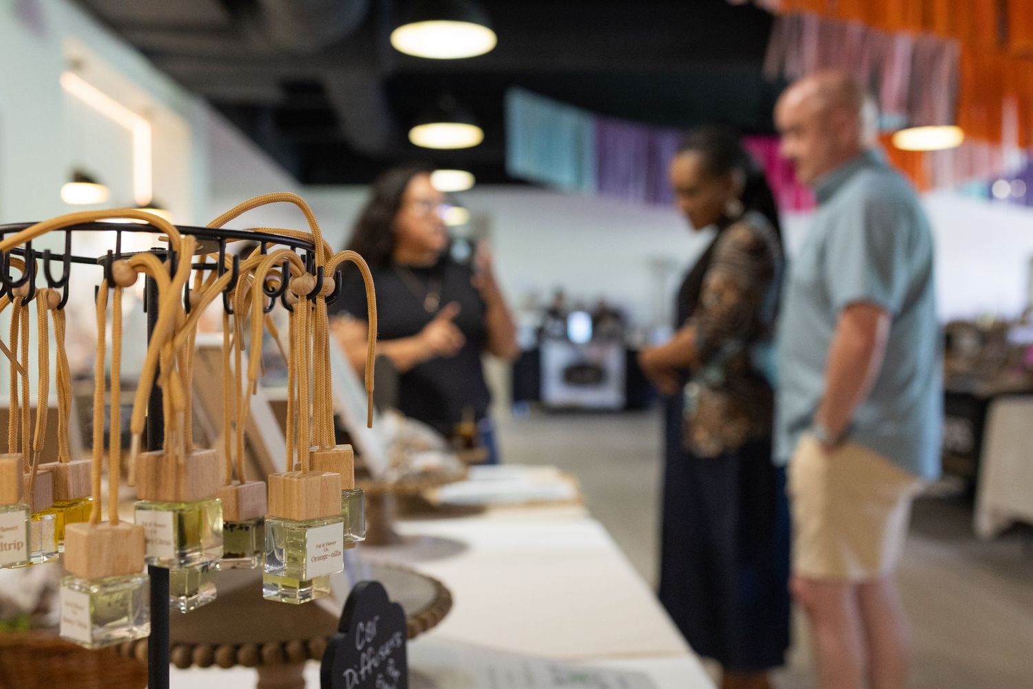 Artisan fragrance bottles with wooden reed diffusers displayed at a vendor table during an indoor market event.