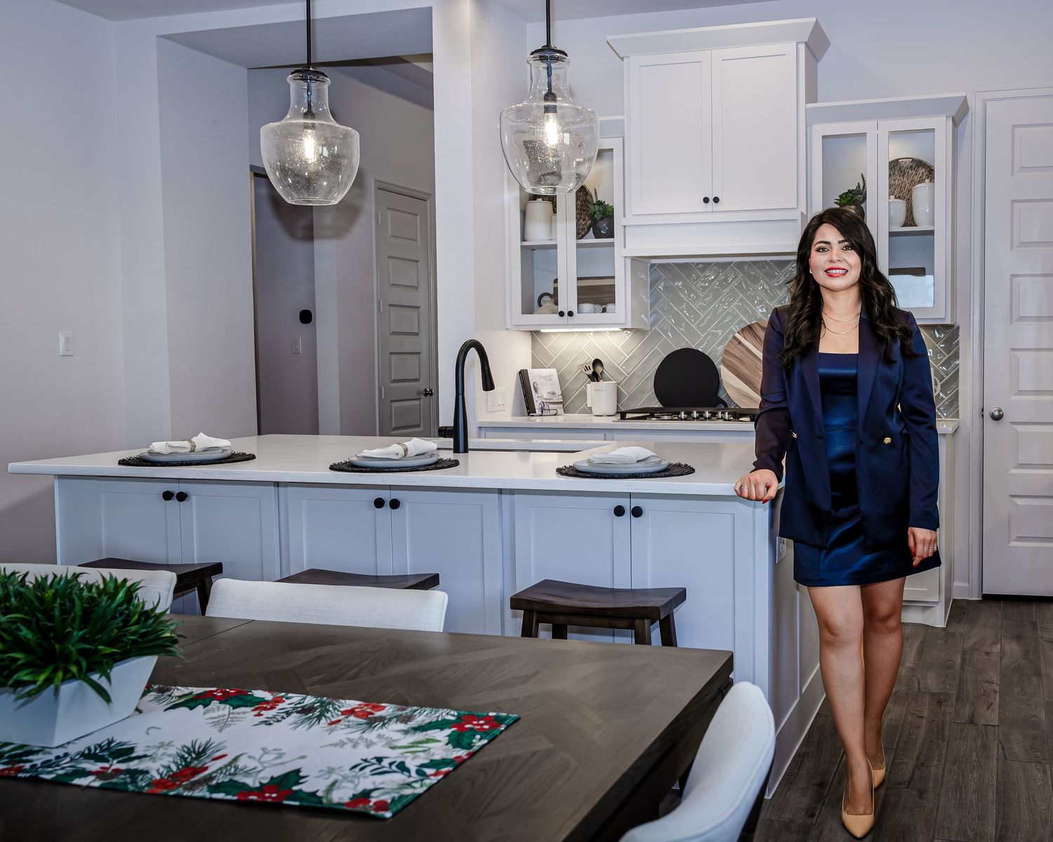 Modern open concept living space with pendant lights, white kitchen cabinets, and dark wood dining table.