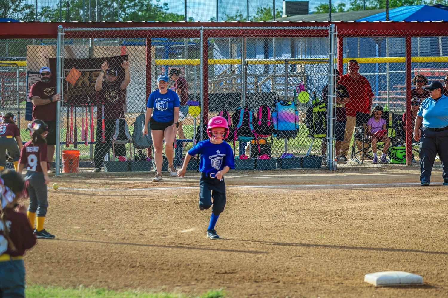 Young girl in pink helmet running bases during a youth softball game on a sunny day.