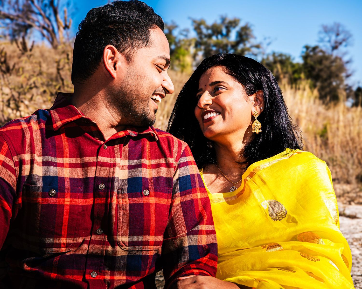 A couple in a red plaid shirt and yellow sweater share tender moments outdoors during a fall photoshoot.
