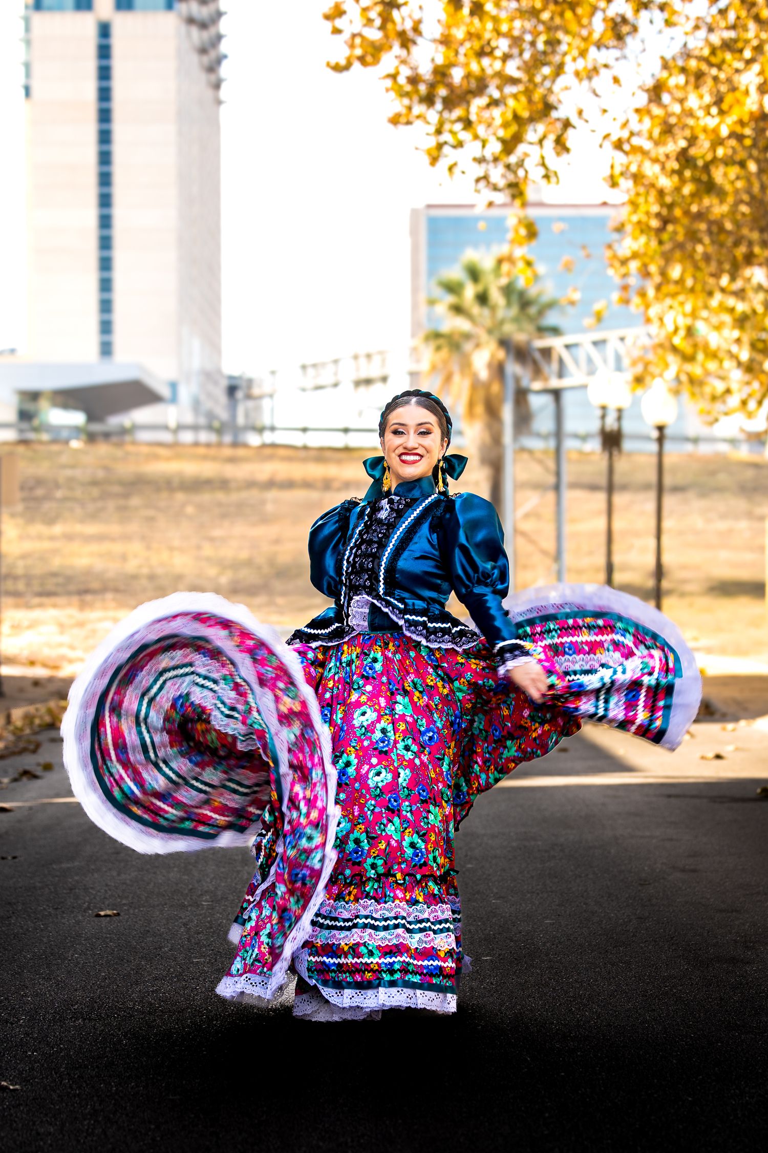 A dancer in a colorful floral dress performs a twirling sequence against an autumn backdrop.