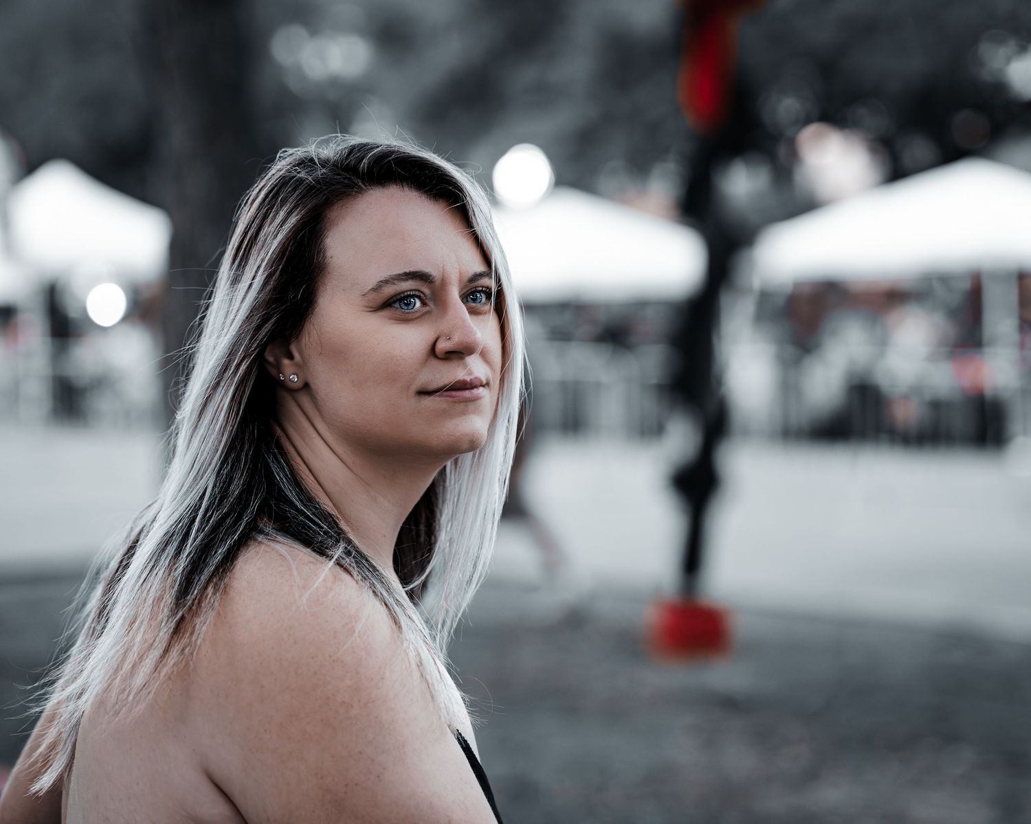 Portrait photo with selective coloring shows someone with long blonde hair looking to the side at an outdoor event.