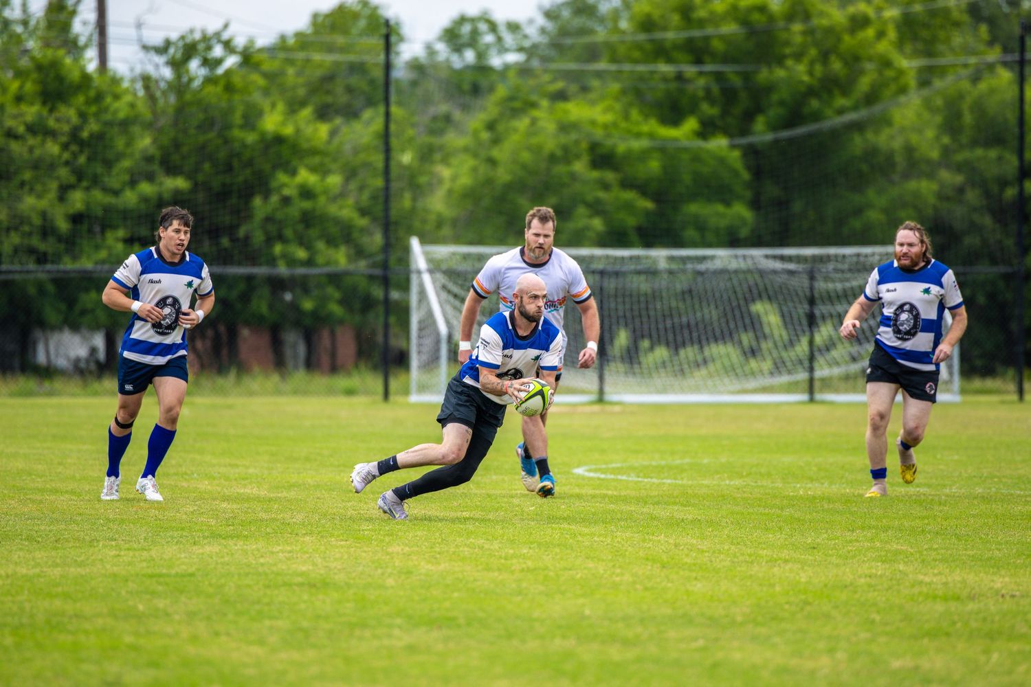 Rugby players compete on a green field during an outdoor match, with one player carrying the ball past defenders.
