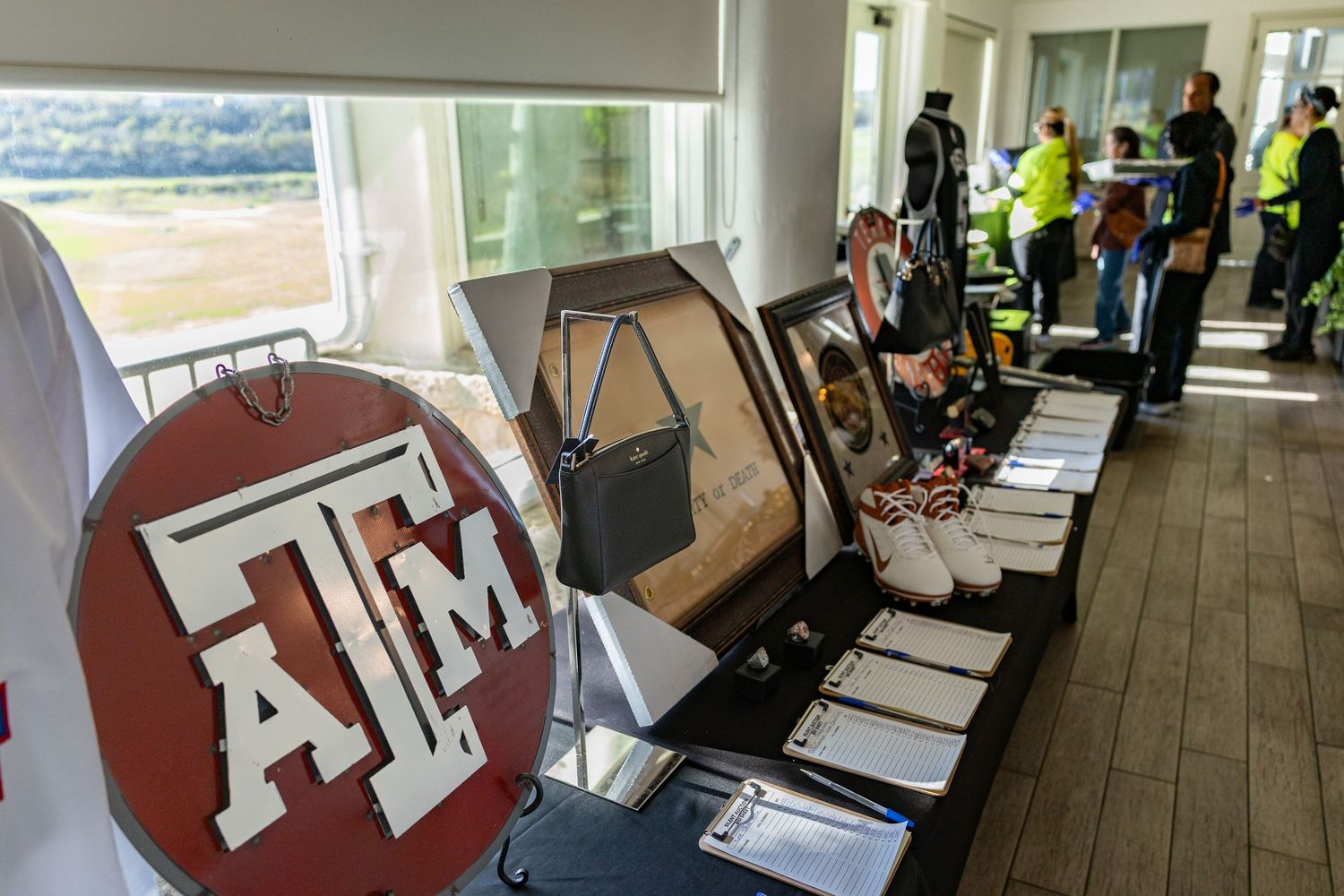 Texas A&M University merchandise and memorabilia displayed on a table at an indoor event with attendees in the background.