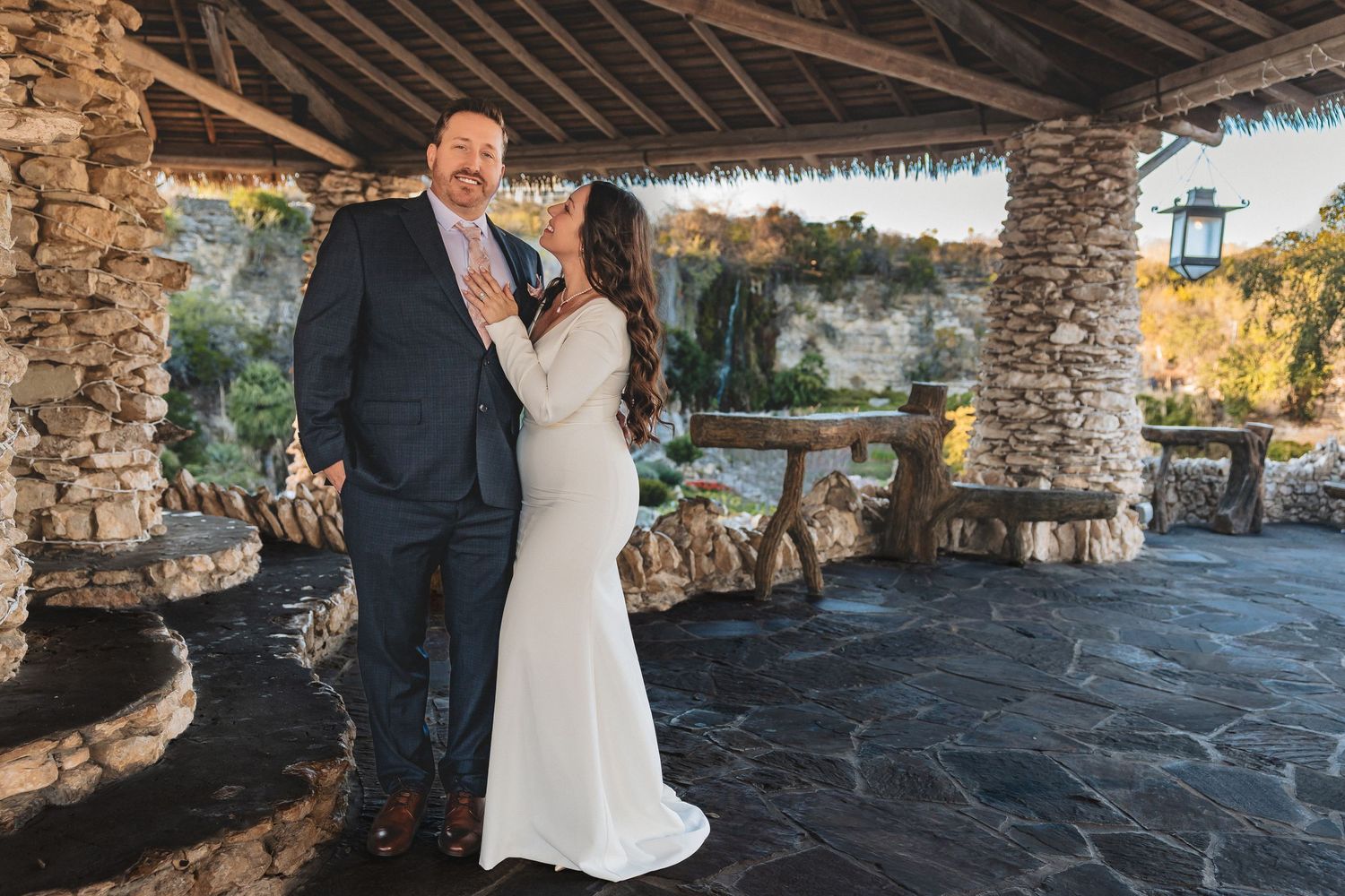 Couple embraces in romantic stone archway during outdoor autumn wedding photoshoot.