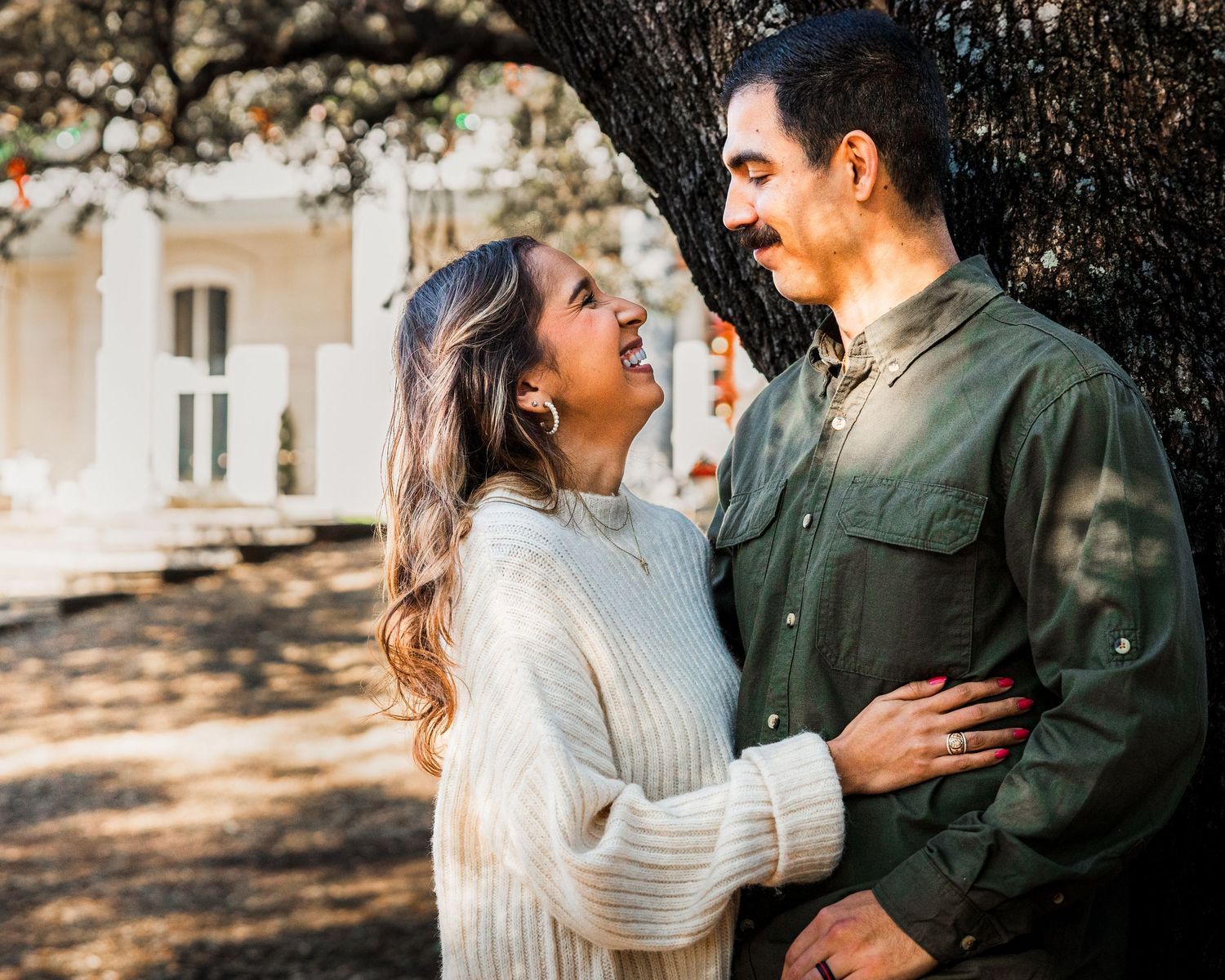 A couple embraces outdoors in warm sunlight wearing casual sweaters during a romantic autumn photoshoot.