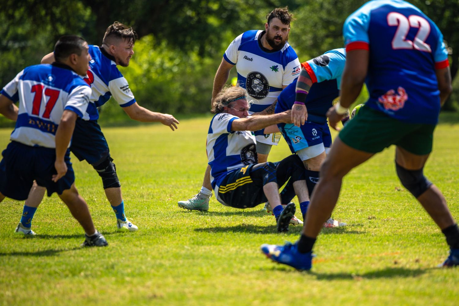 Rugby players compete in a dynamic tackle during an outdoor match on a sunny day.