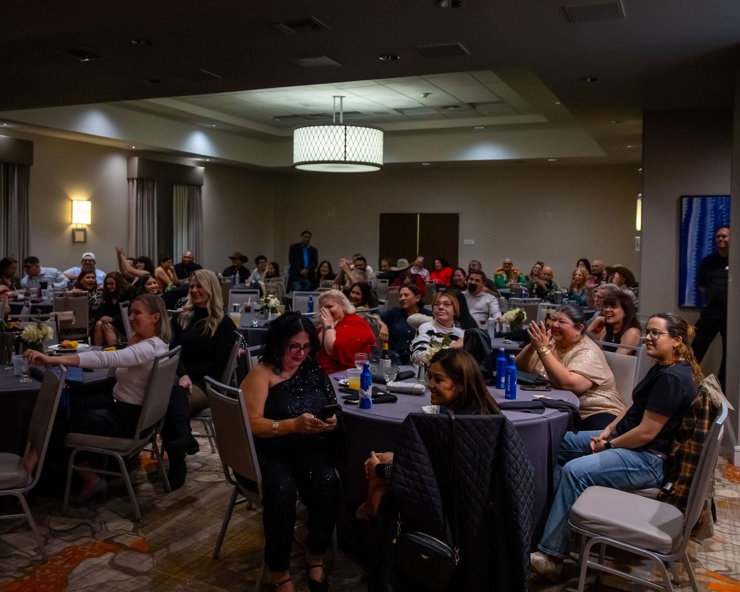 Crowd of people seated at round tables in a banquet hall during an evening event or conference.