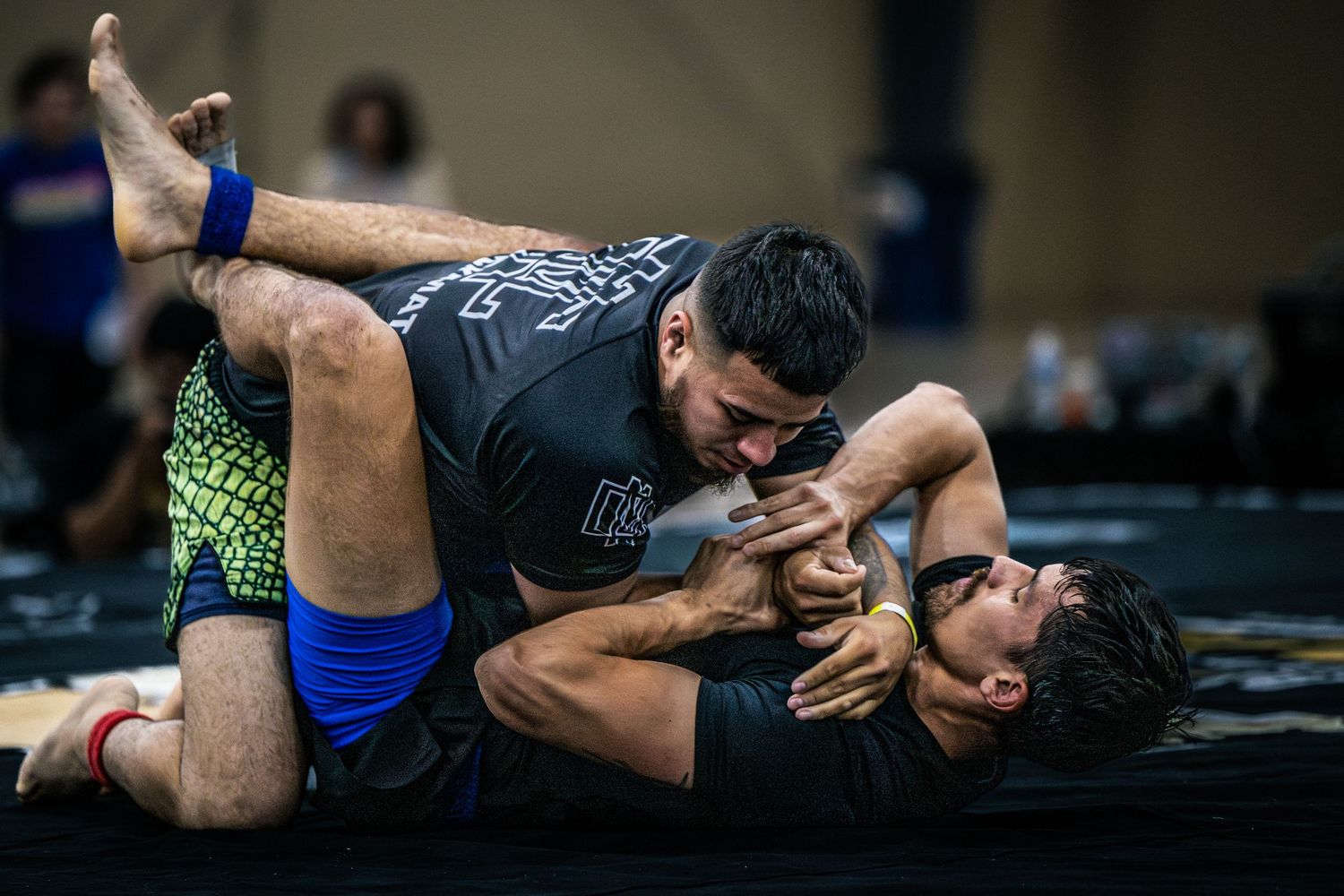 Two athletes competing in a grappling match on a mat during a Brazilian jiu-jitsu or wrestling tournament.
