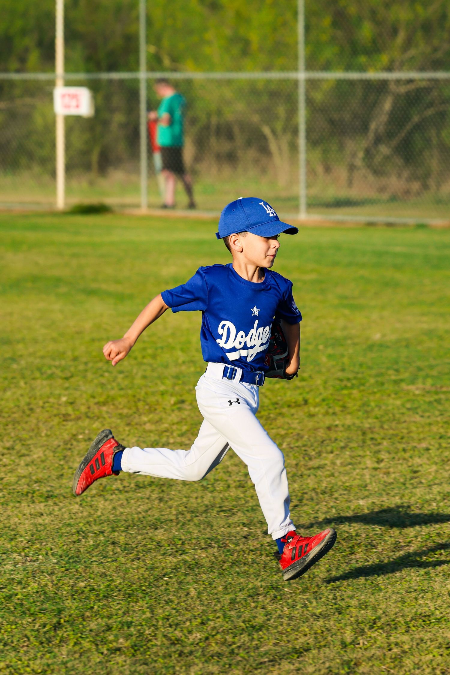 Young boy in Dodgers baseball uniform running on green field during little league game.