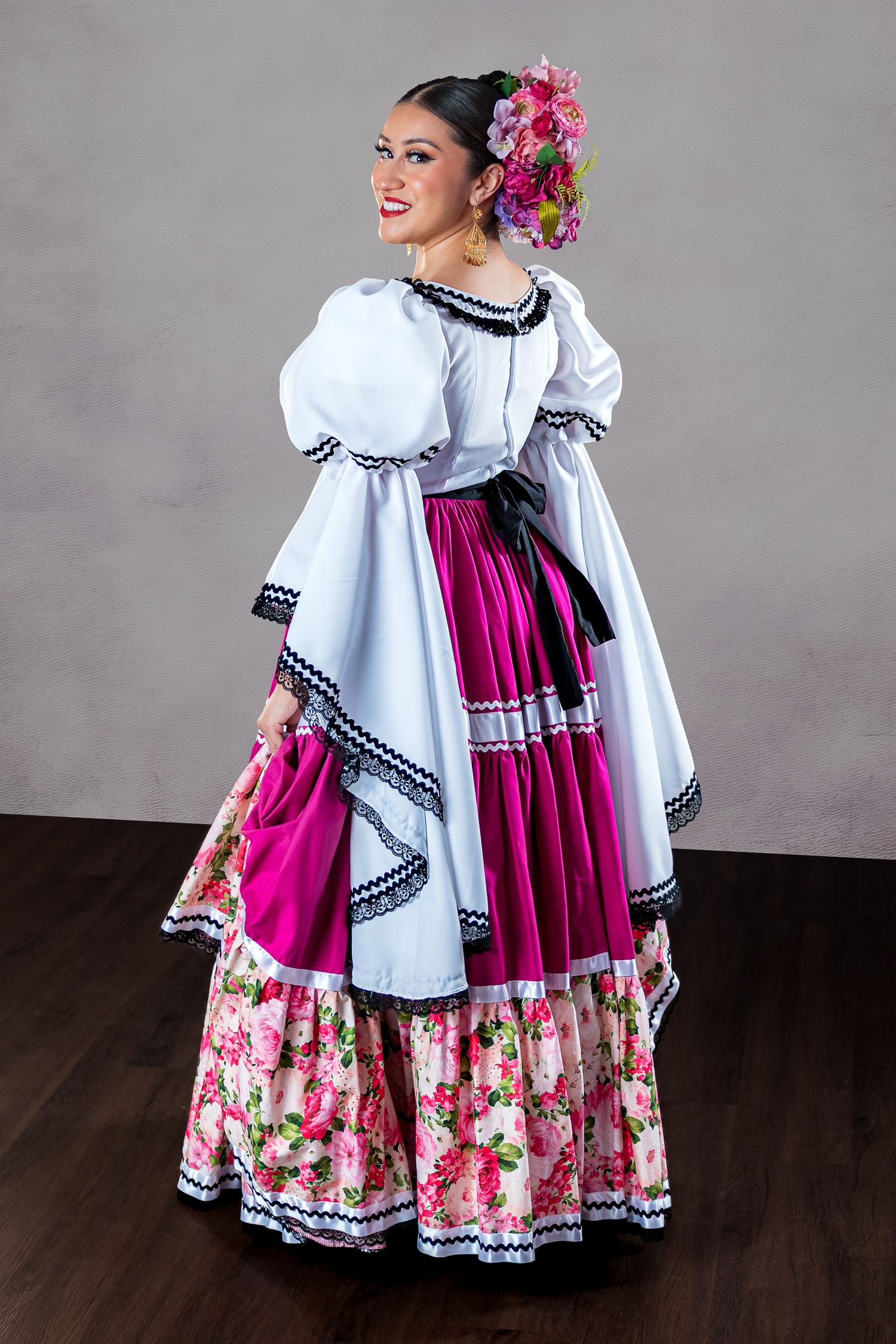Traditional folk dancers in white and pink floral dresses with black trim perform a spinning movement on dark floor.