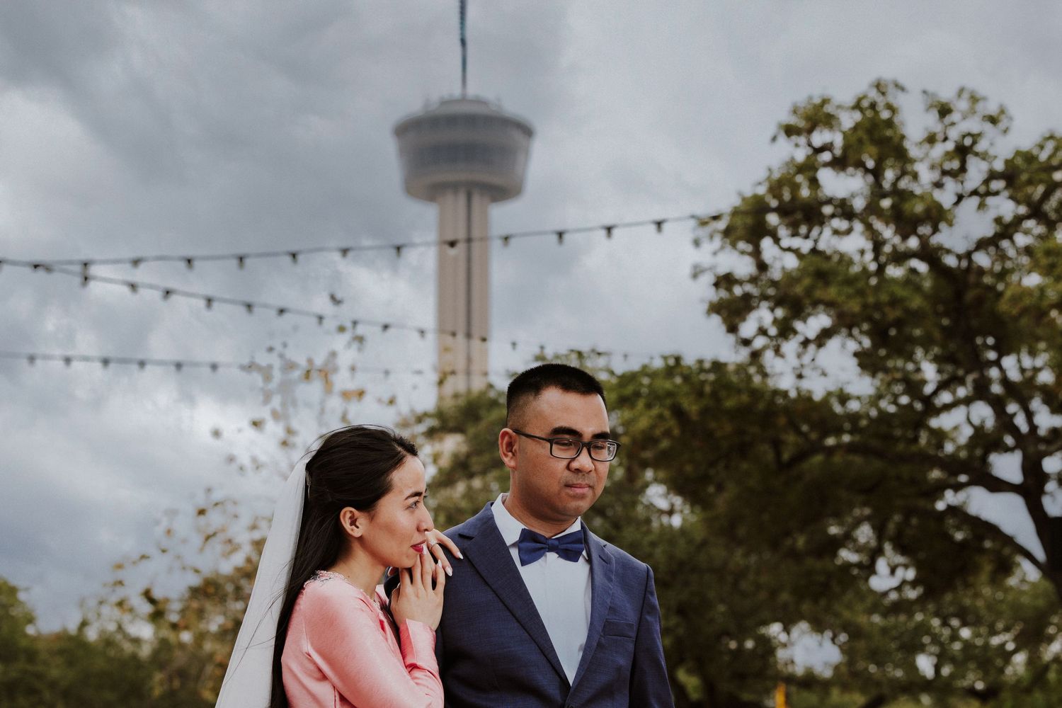 A couple shares an intimate moment under string lights at an outdoor wedding reception during sunset.