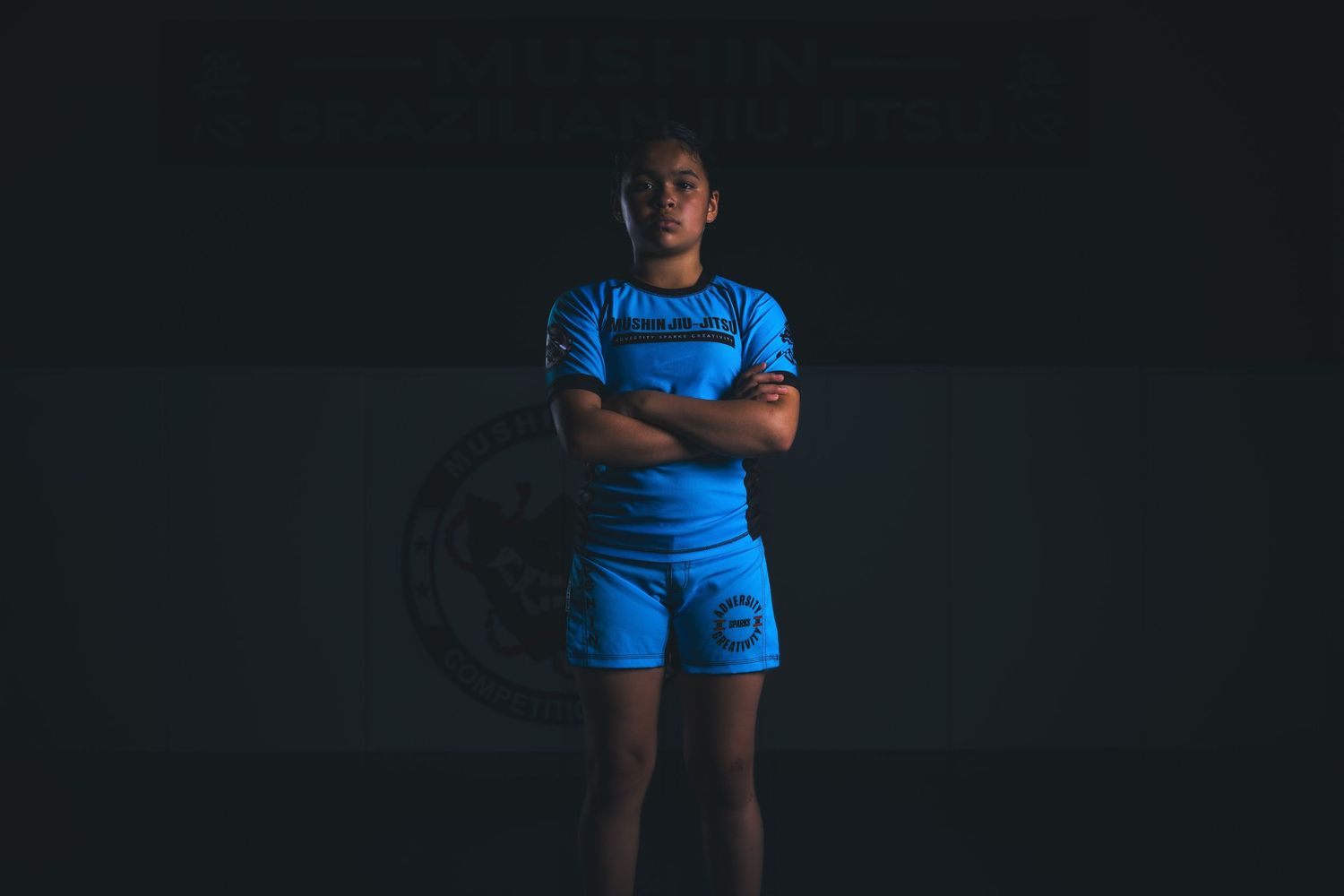Athlete in blue athletic wear stands confidently with arms crossed against a dark background.