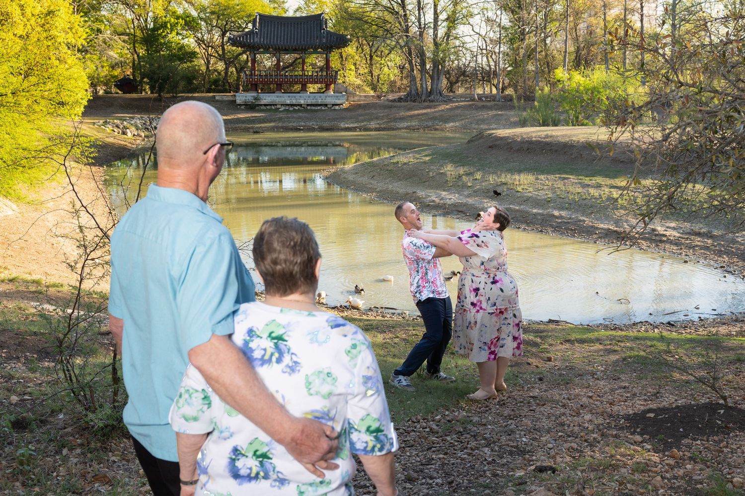 A group of people walking along a path near a pond in a wooded area.