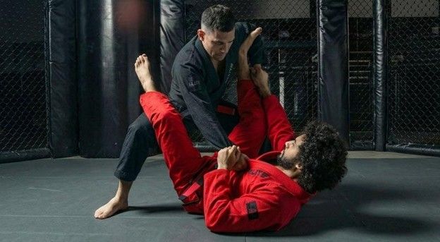 Two BJJ practitioners sparring on a mat, one in black gi applying guard pass against opponent in red gi.