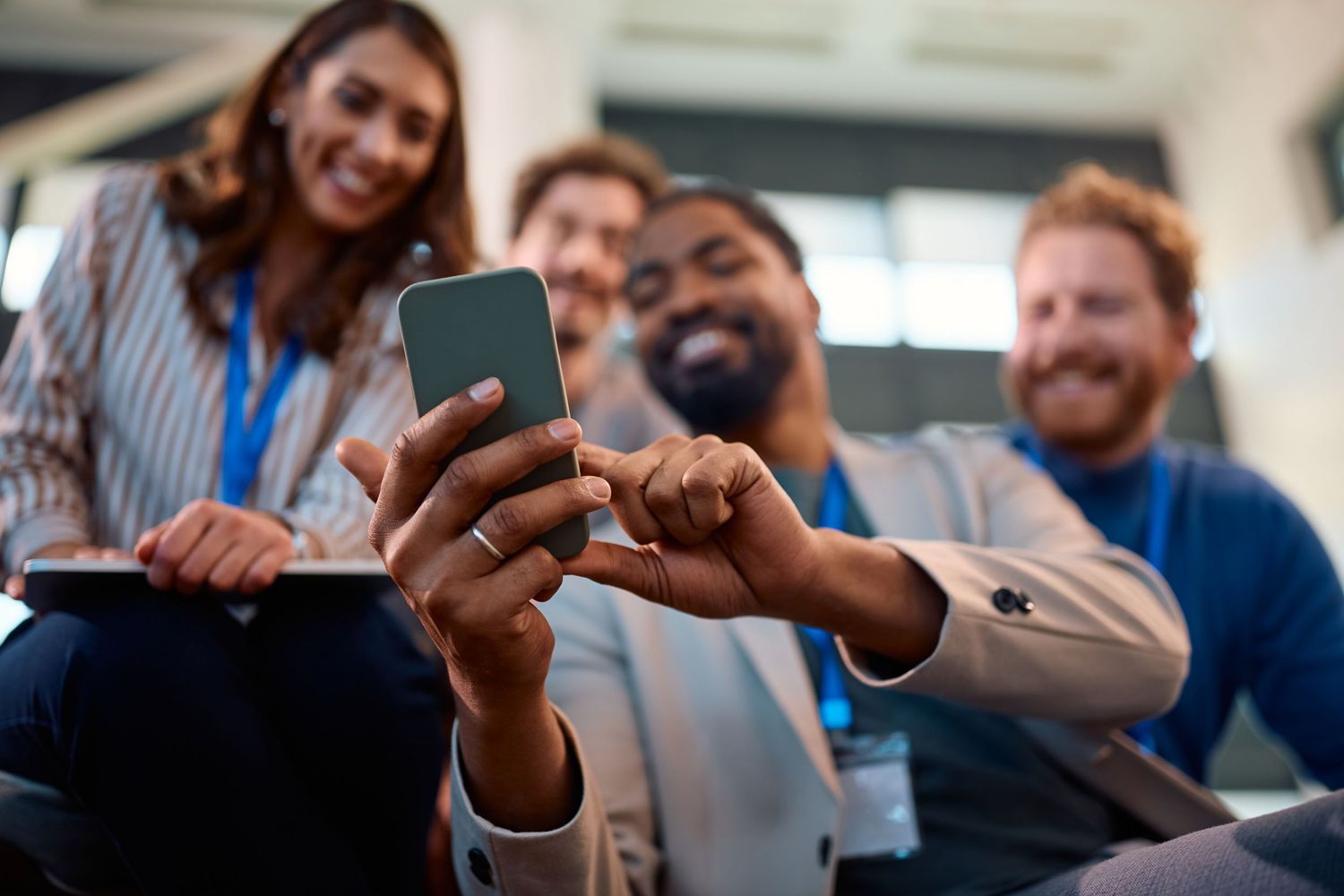 Diverse group of smiling business professionals sharing content on a smartphone at a conference event.