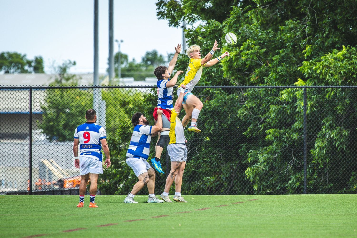 Rugby players compete in a lineout during an outdoor match, with one player lifted high to catch the ball.