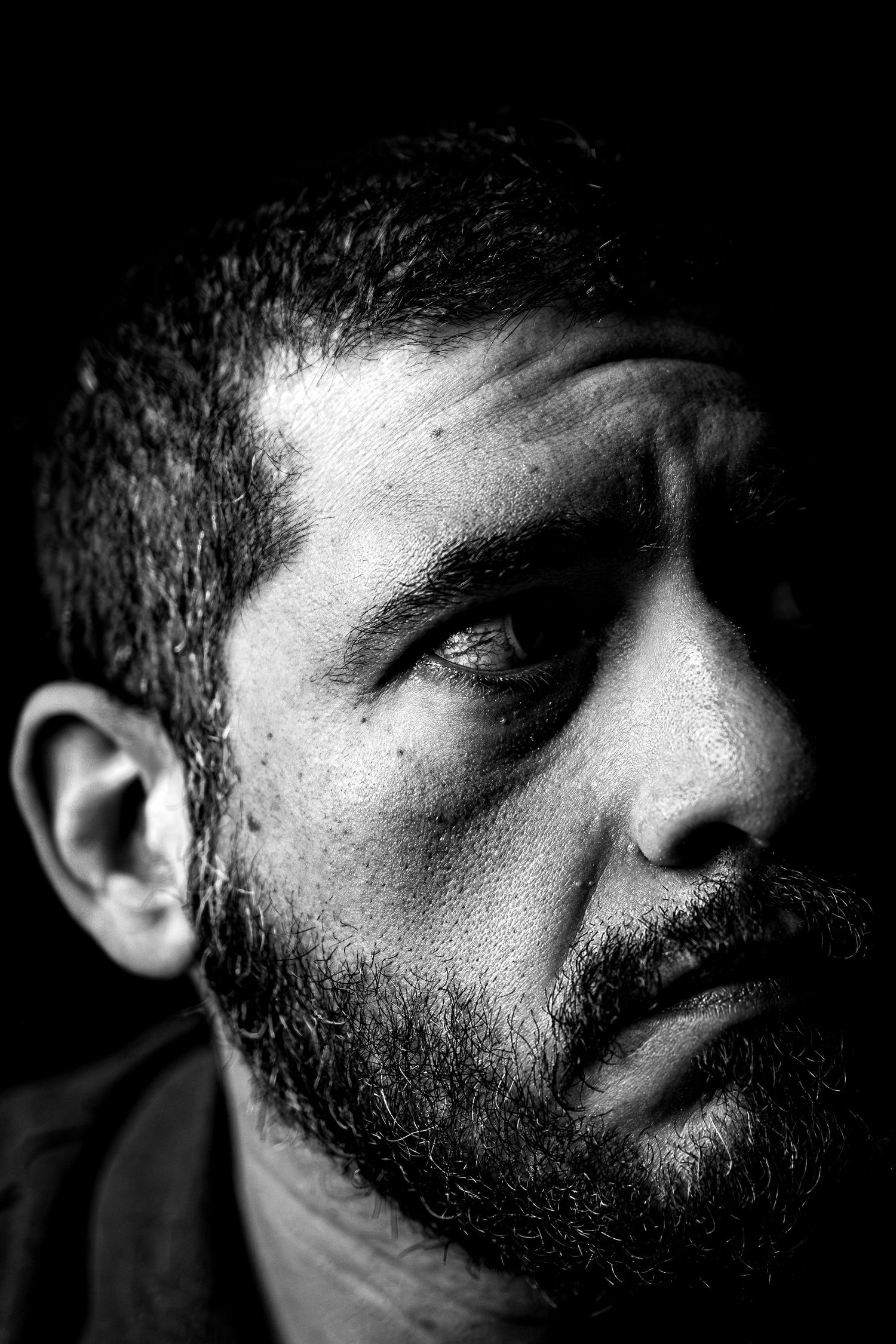 Close-up black and white portrait of bearded man with dramatic shadows.