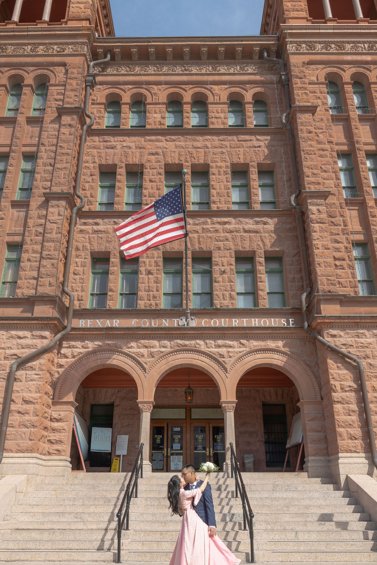 Historic red sandstone courthouse building with American flag and grand arched entrance.