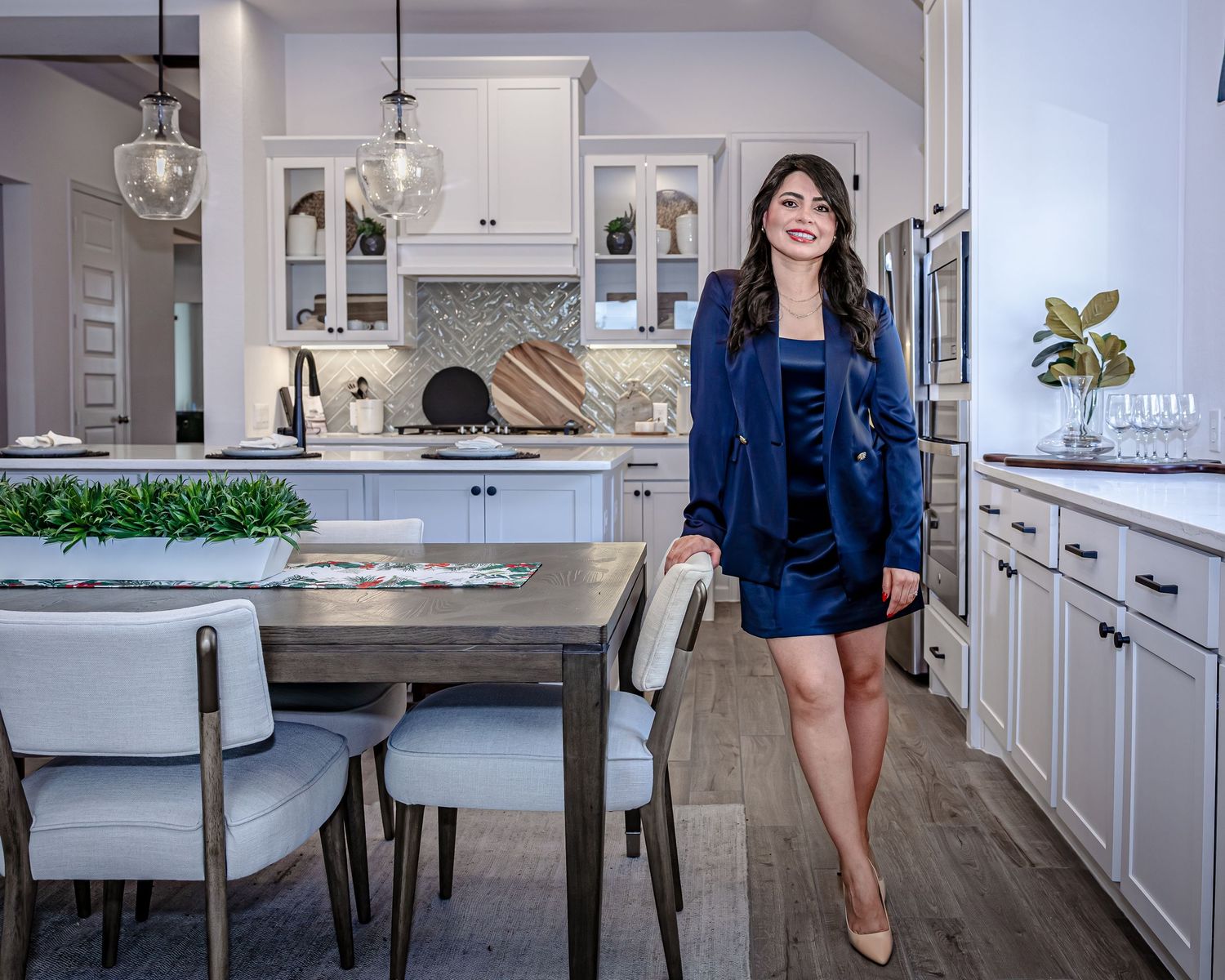 Modern white kitchen with hardwood floors features pendant lighting and navy blue accents throughout the design.