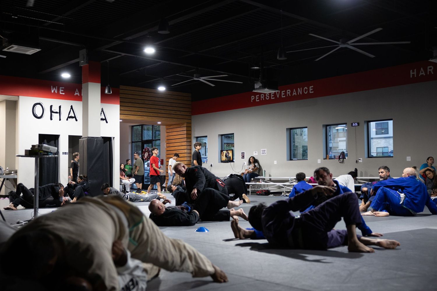 BJJ students practicing ground techniques on mats in a martial arts gym with Ohana branding on the wall.