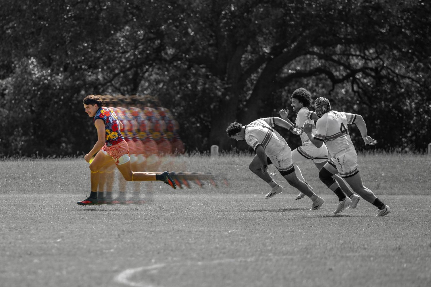 Rugby players chase a colorful opponent in a selective color sports action photo.