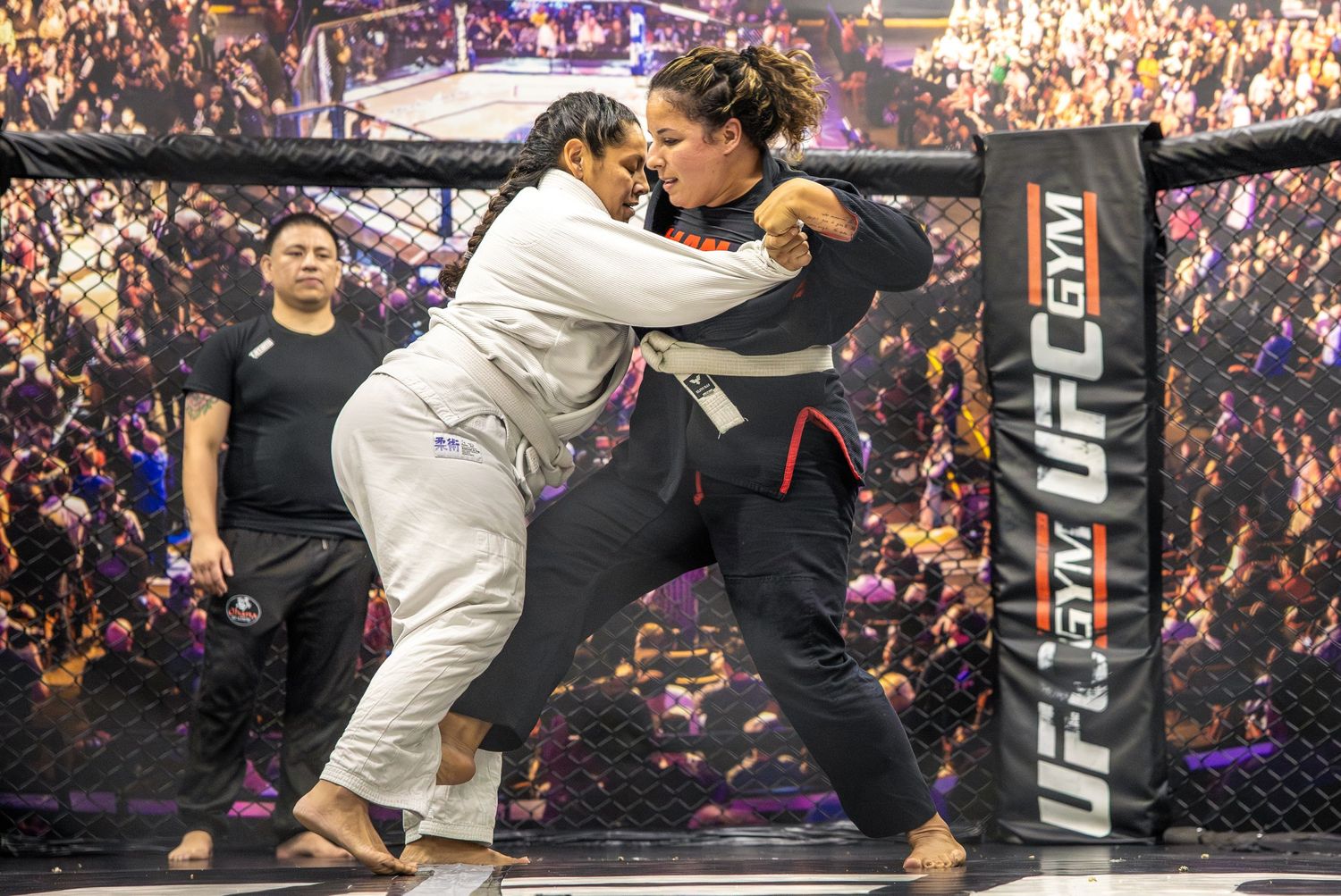Two women grappling in a UFC Gym MMA cage match during a competitive martial arts bout.