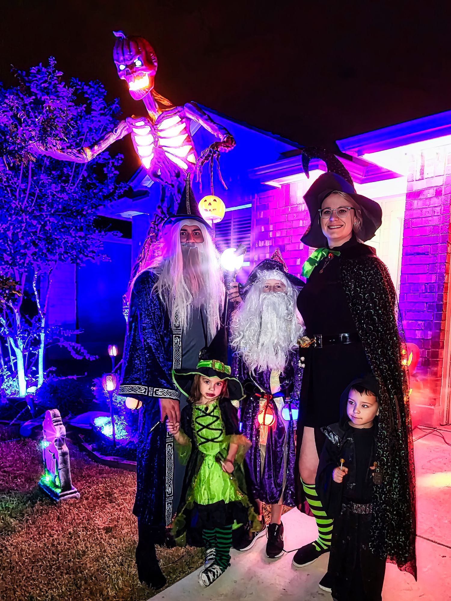 Halloween decorated house with spooky lighting, glowing skeleton prop, and group in witch and wizard costumes standing outside.