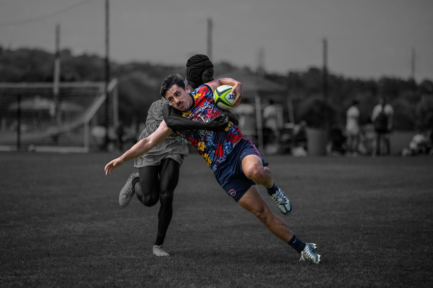 Two rugby players compete for the ball during an intense match on a grass field, captured in selective color photography.