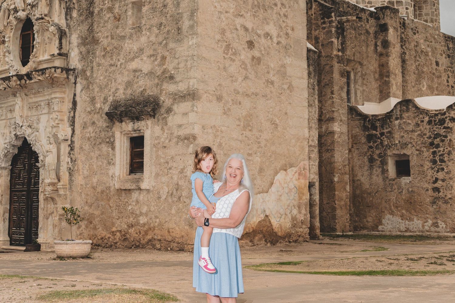 Woman holding young child in front of historic stone mission building in San Antonio, Texas.