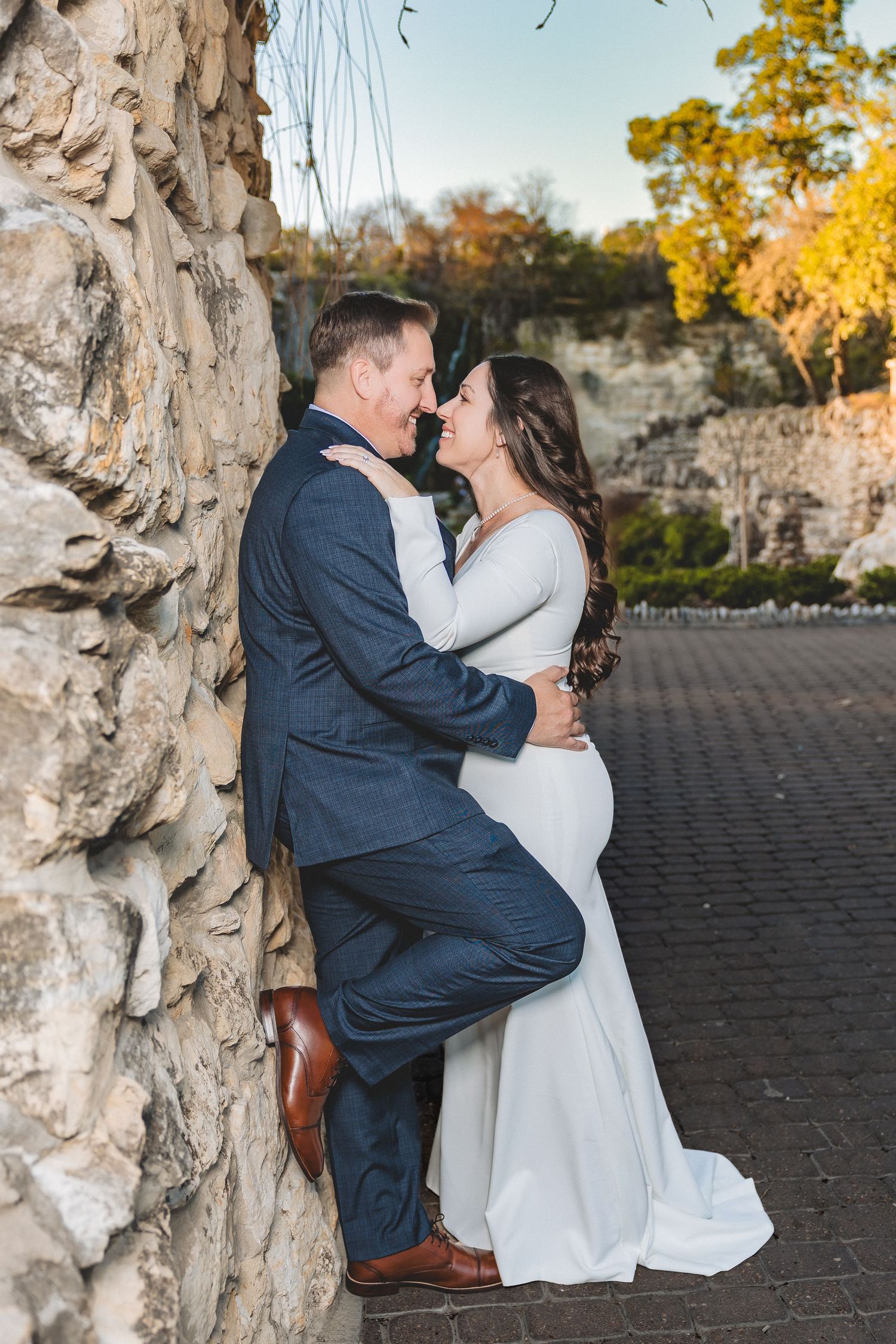 A couple shares a romantic kiss outdoors in front of a stone wall during an autumn wedding photoshoot.