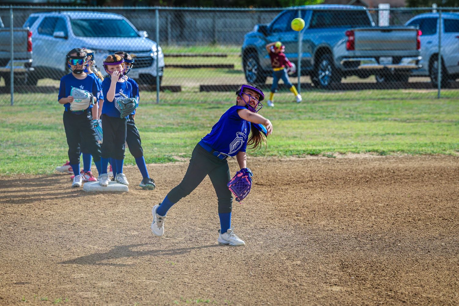 Young softball pitcher winding up to throw during a youth league game with teammates in background.