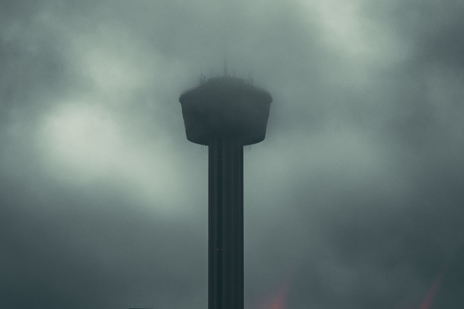 Dark water tower silhouetted against stormy gray clouds in a moody sky.