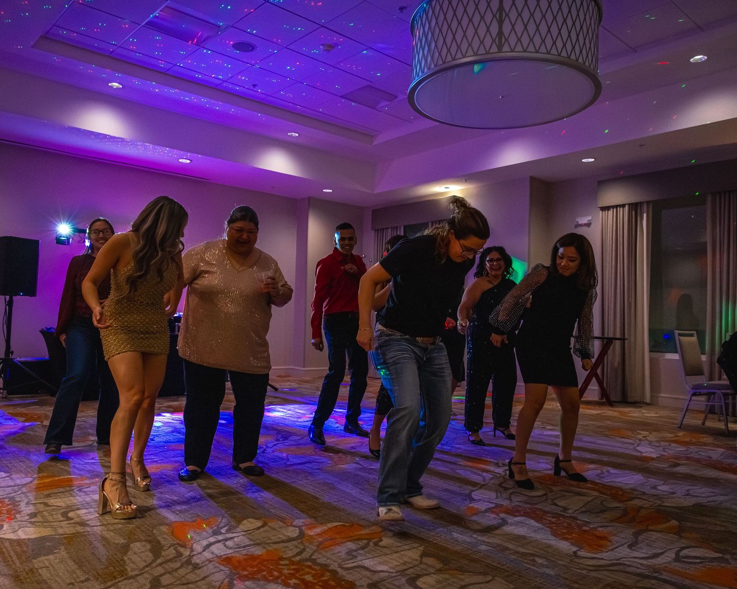 Group of people dancing at an indoor party with purple ambient lighting in a hotel ballroom.