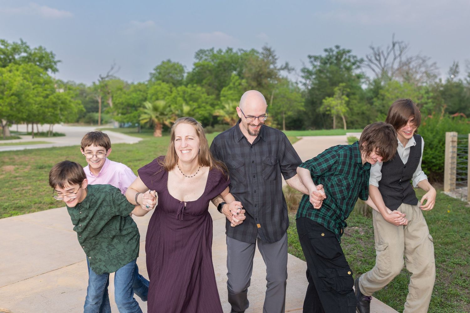 Happy family of six holding hands and laughing together outdoors in a park on a sunny day.