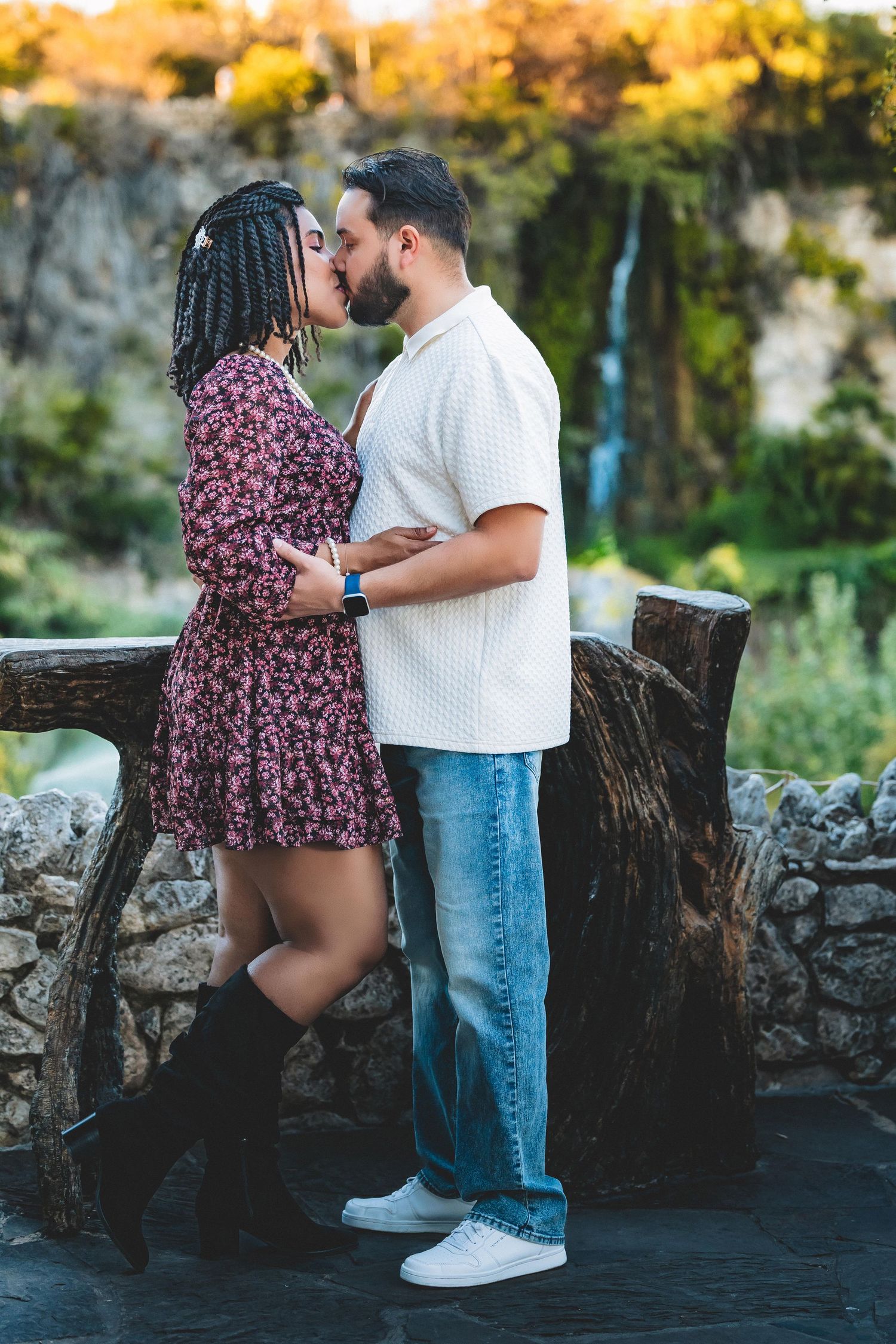 A couple shares an intimate moment against a rustic stone wall backdrop during golden hour.